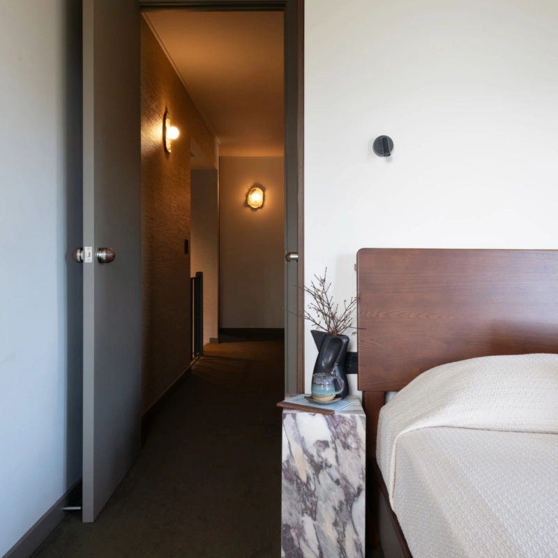 1970s-inspired bedroom featuring soft neutral walls painted in Aalto Endless, a timber bedhead, marble bedside table and warm hallway lighting.