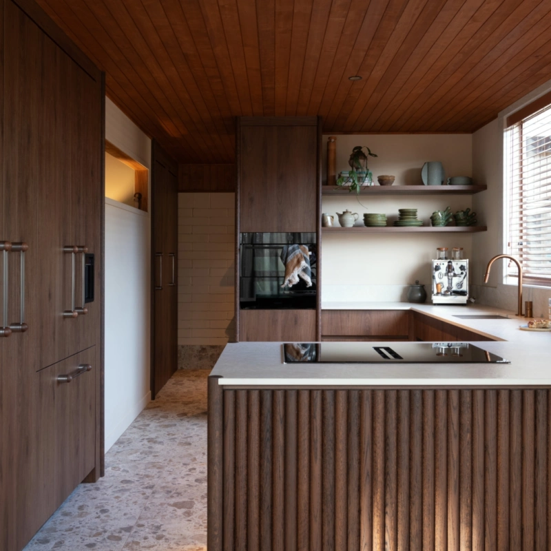 1970s-inspired kitchen featuring warm neutral walls painted in Aalto Clayware, rich timber cabinetry, timber-lined ceiling and stone benchtops.