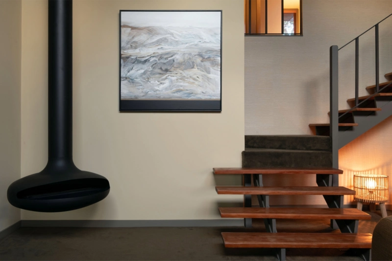 Living room featuring warm neutral walls painted in Aalto Compatible, a black suspended fireplace and timber staircase.