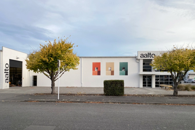 Street view of Aalto Paint's Christchurch store, featuring promotional paint posters and landscaped trees.